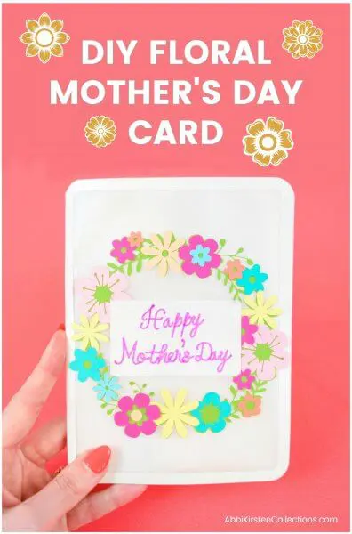 A hand holding a Mother's Day card with a floral wreath on the cover.
