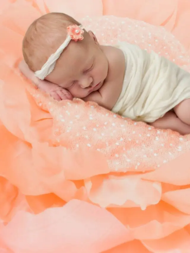 A baby sleeping on a peach colored giant crepe paper flower