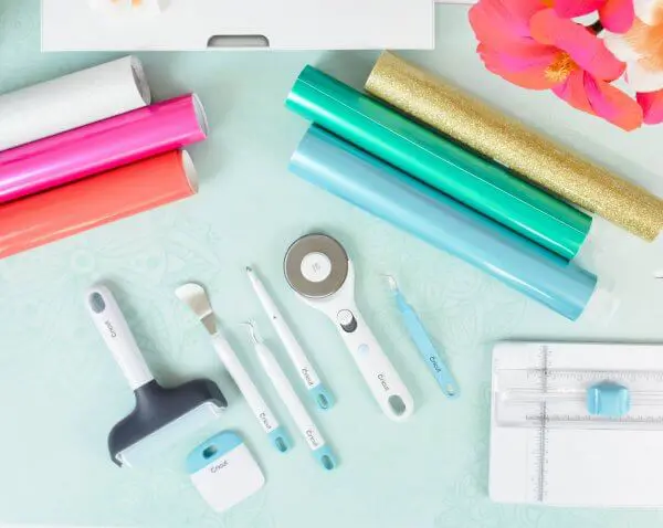 A tabletop full of crafting supplies like vinyl rolls and Cricut cutting tools.