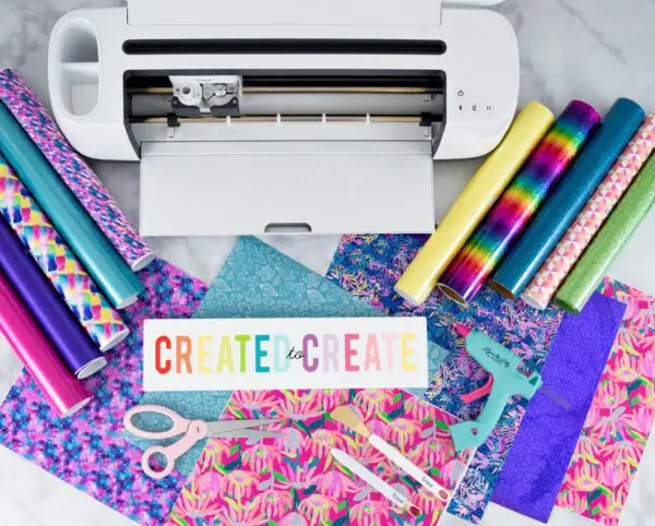 Cricut maker machine open on a desk with cricut vinyl and other tools and materials around.