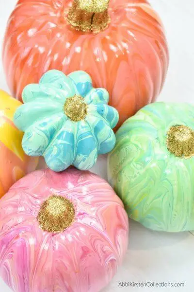 Orange, green, pink, blue and yellow painted pumpkins in varying sizes and shapes against a white background. 
