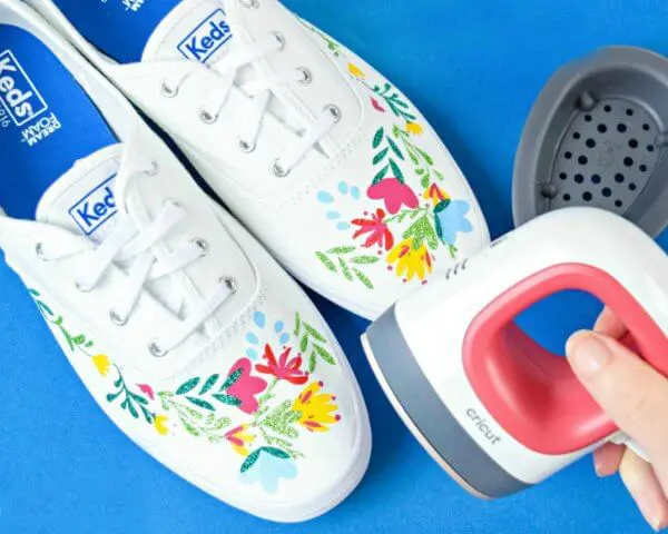 An Easypress mini for shoes next to white sneakers with iron-on vinyl floral stickers on the toes. Vinyl is easy to use with these Cricut hacks.