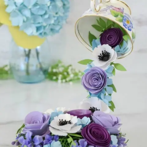 A floating tea cup with cascading purple, white, and blue paper flowers.