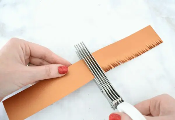 Abbi demonstrates how to use fringe scissors to cut a brown strip of cardstock to make the sunflower center. 