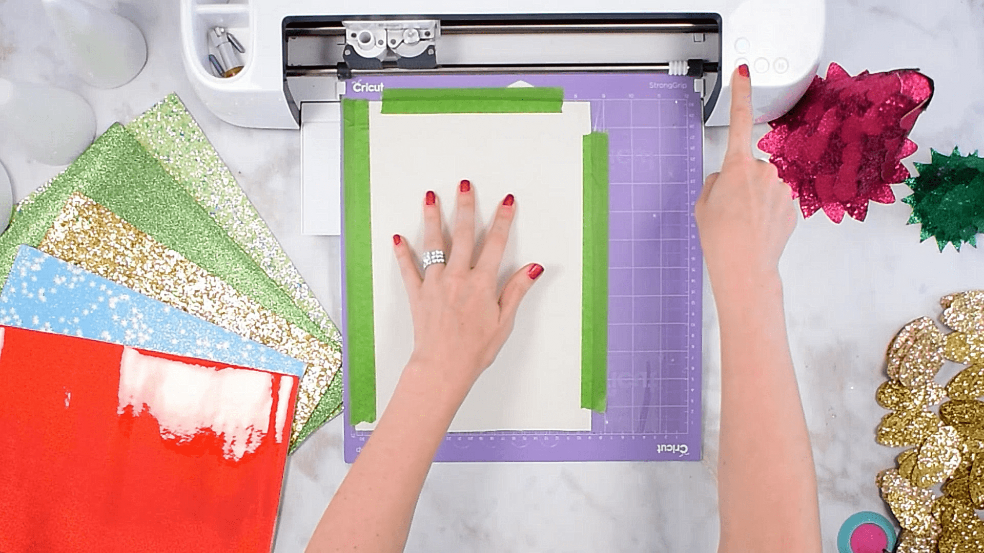 In an overhead view, Abbi Kirsten's arms are visible as she demonstrates how to cut chunky glitter leather on your Cricut machine. The glitter leather sheets are on her left, and she has taped down the faux leather on her Cricut mat before she loads it into her Cricut machine.
