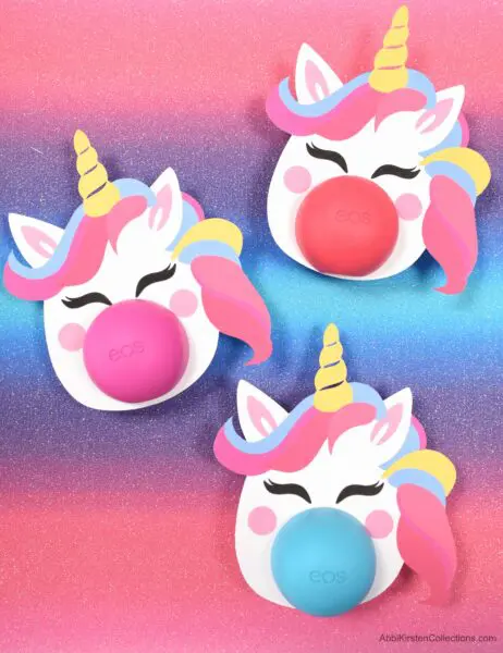Three happy, colorful unicorn heads have Eos lip balm as noses. These templates are available for free and make great gifts.