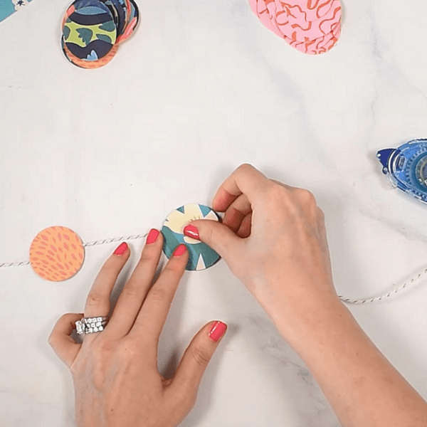 Gluing green and yellow wrapping paper circles onto white twine to create a banner. 