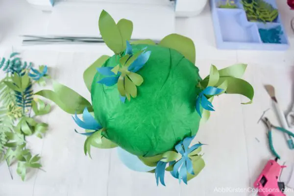 The green tissue paper-wrapped foam ball has various greenery added to it.