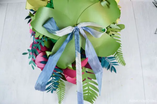 A thin blue and white ribbon is wrapped around the bouquet handle and tied in a bow.
