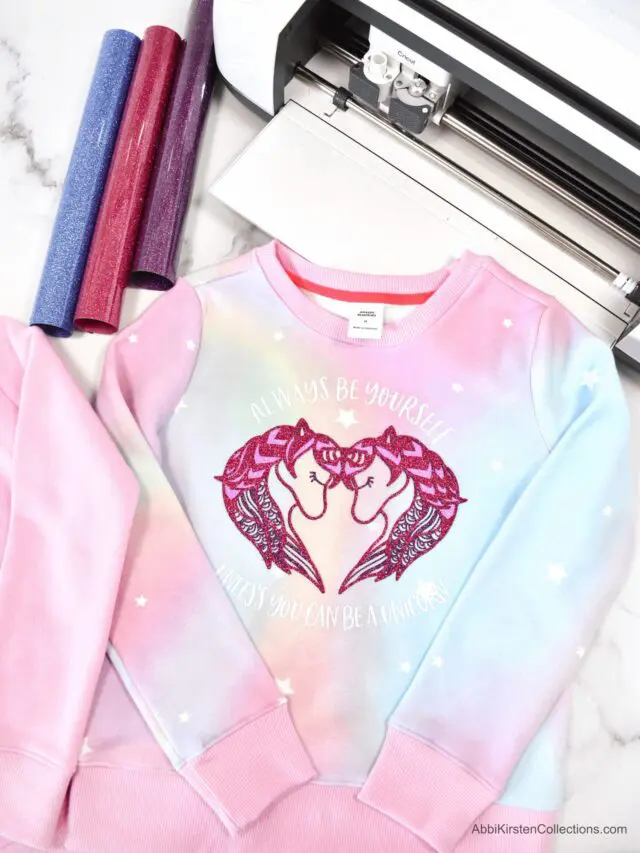 A pink and blue ombre long sleeve top with two unicorn heads forming a heart shape print