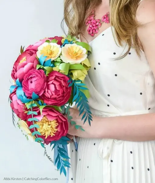 Side view of a woman in a white dress holding a colorful DIY cascading paper flower bouquet that can be used as an alternative to live flower bouquets in weddings and other special events.