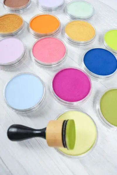 Multiple colors of inks and pan pastels along with a stamper on a white table. 