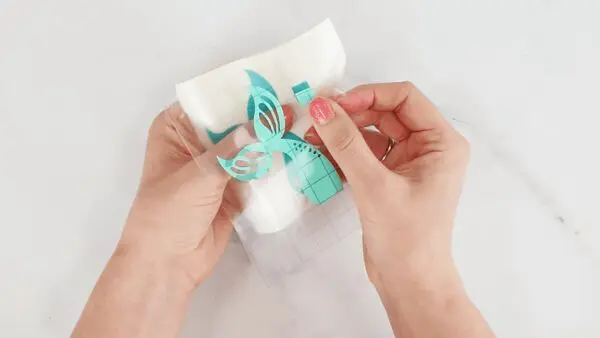 A closeup of a woman's hand layering transfer tape and a vinyl mermaid's tail using parchment paper. One of many vinyl hacks for Cricut crafts.
