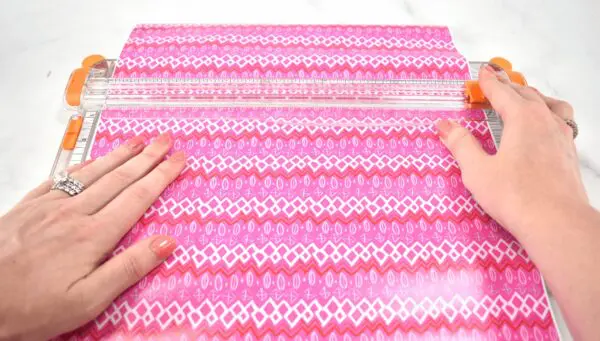 A woman's hands load a pink patterned vinyl sheet into a clear craft cutter. Use these 25 vinyl hacks when crafting with your Cricut machine.