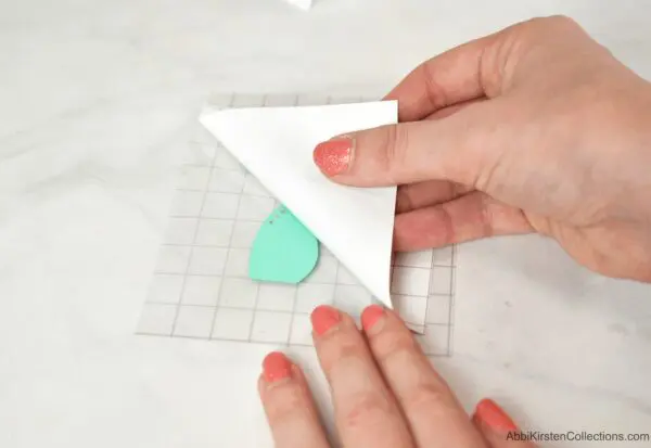 A closeup demonstration of how to lift your liner from the transfer tape. A woman's hands gently remove the liner from the vinyl. One of 25 hacks to make crafting with your Cricut machine and vinyl more fun.