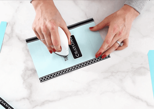A close-up of Abbi's hands ironing on black vinyl on to the outside paper of a light blue crayon using an Easypress mini.