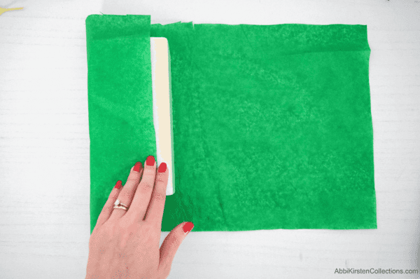 An image sows Abbi covering a while floral foam block with green tissue paper to make a poinsettia flower arrangement.