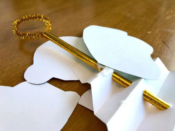 The paper angel craft is turned over to glue the angel wings onto the back of the gold paper straw running through the decoration.