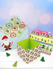 A DIY gingerbread man Holiday explosion card with a bright green interior next to a blue and gold striped envelope on a white table. 