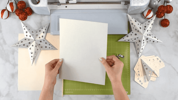 Abbi holds a piece of white cardstock near a Cricut machine. Two paper stars lay near by.