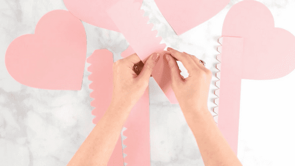 Pink paper heart box templates being folded on top of a marble workstation.