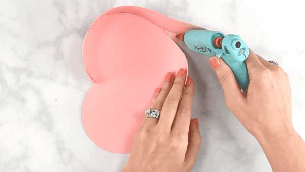 Hot glue being applied to the edges of a pink paper heart.