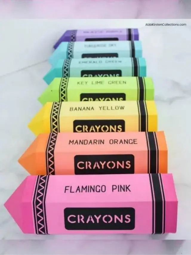 Six crayon paper box crafts lined up in a marble countertop. In front is pink, followed by orange, yellow, teal and light blue.
