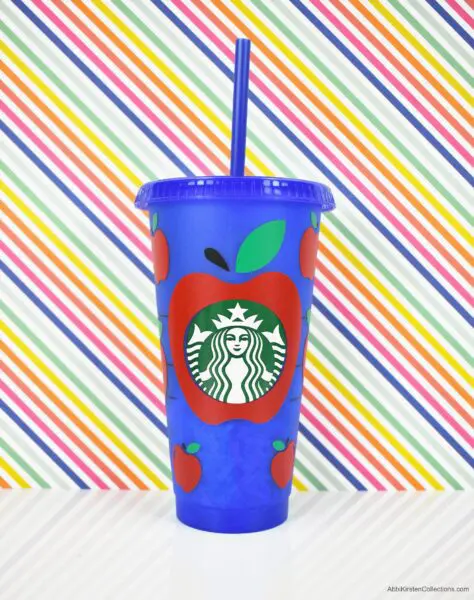 A blue plastic reusable Starbucks cup with an apple vinyl decal. A large apple surrounds the Starbucks logo, with smaller red apples around it.