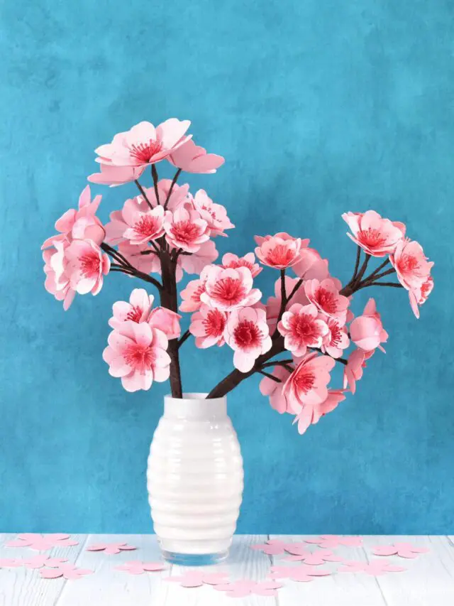 Paper cherry blossoms on a white vase against a blue background.