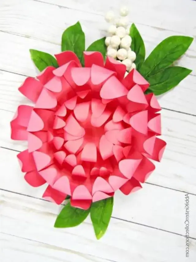 A flat lay photo of a pink paper chrysanthemum with green paper leaves.