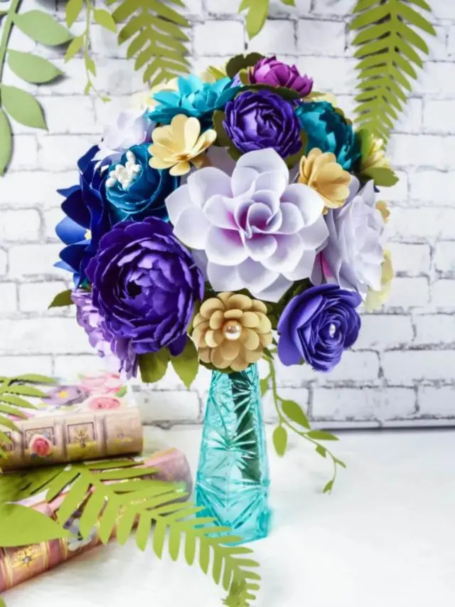A bouquet made of assorted paper flowers in different shades of purple and teal, arranged in a clear teal vase.