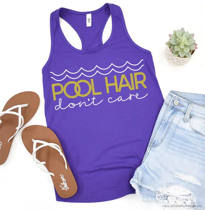 A racerback blue tank has vinyl waves and the text "Pool Hair Don't Care" on the front. Sandals, a succulent, and folded, faded denim shorts round out the picture.