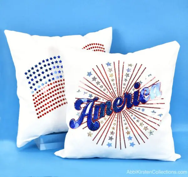 Two July 4th pillows with iron-on sparkle holographic vinyl sit on a light blue background. One pillow has an American flag design, and the other has a firework with the word "America" bursting in the foreground.