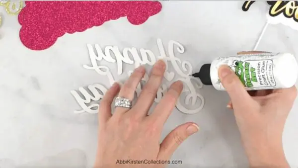 A pair of hands squeeze Bearly Art glue on the back of a "happy birthday" sign.