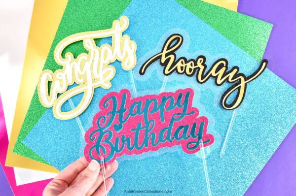 Three colorful signs that read "congrats", "hooray" and "happy birthday" laying on multicolored pieces of paper.