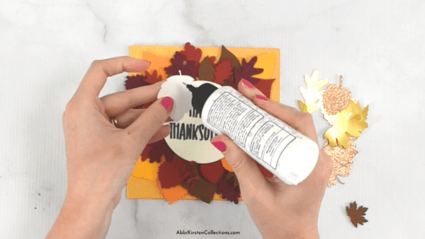 Hands adding Bearly Art glue to the back of paper leaf cutouts. 