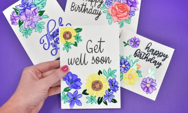 Cricut Watercolor Markers and Brush Set are perfect for paper crafts and DIY cards. These cards on a deep blue paper background are hand-made and can be used for any occasion like these which say "Get Well Soon," "Happy Birthday," and "Thank You." Abbi holds the Get Well card decorated with printed yellow flowers. 