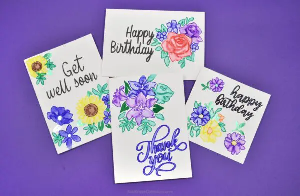 Another overhead view of finished greeting cards made with Cricut Watercolor accessories. The four cards are laid out on a deep blue background. 