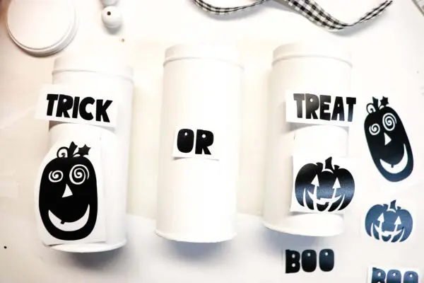 An overhead view of how to apply the vinyl to the three repurposed, painted cookie tins. The words include "trick or treat" and "boo," and fun pumpkins. 