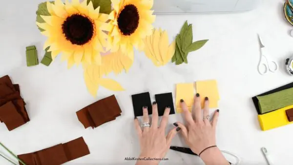 A bunch of crepe paper sunflowers sit above the pieces and petals of the sunflower craft.