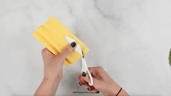 Abbi Kirsten's hands cut sunflower petals out of a piece of yellow crepe paper using detail scissors and her template.