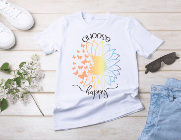 Tennis shoes, jeans, sunglasses, and flowers lay on white wood with a white t-shirt in the middle. The t-shirt has a rainbow-colored sunflower with the left side turning into butterflies. The black text on the shirt says, "Choose Happy."