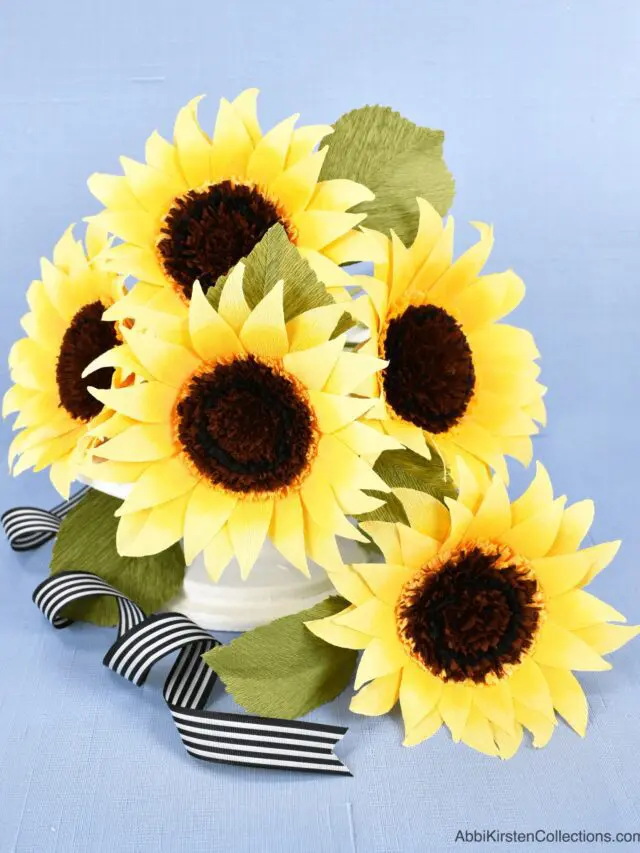 Five crepe paper sunflowers with green crepe paper leaves on a white vase