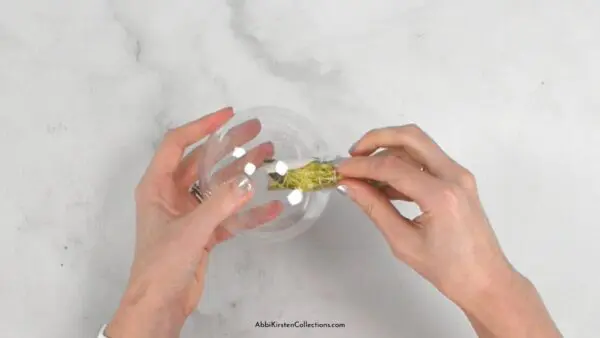 Photo cut out being inserted into a clear plastic ornament