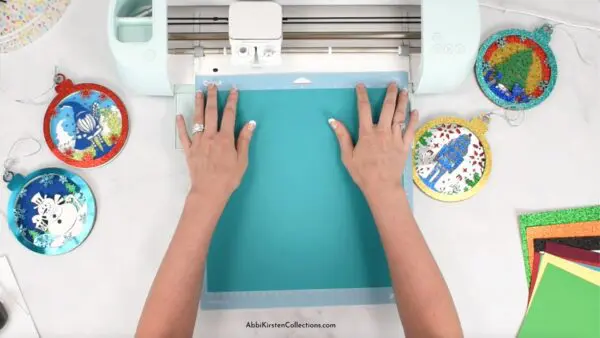 Image shows teal cardstock paper being cut on a Cricut machine.