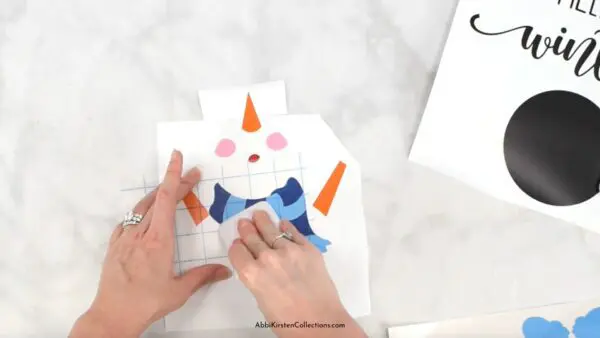 A close-up of Abbi Kirsten's hands burnishing the layers of vinyl on to transfer tape to be placed on a circular piece of wood. 