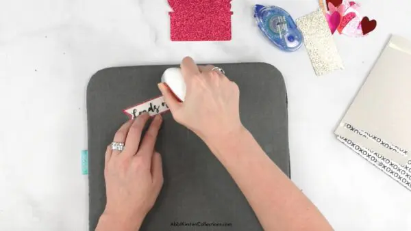 Abbi Kirsten's hands press iron-on vinyl onto to cardstock for a DIY Valentine's Day card with Cricut.