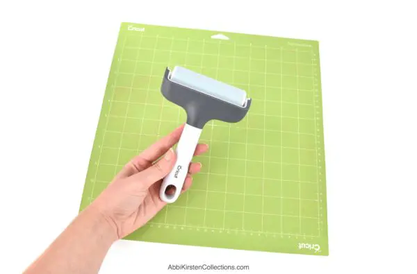 The image shows a green Cricut mat with a Cricut brayer tool used to press materials to the mat for the best cutting results.