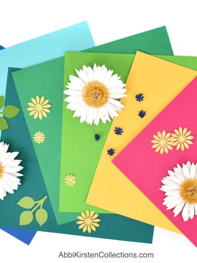 The image shows colorful cardstock with paper flowers on a desk.