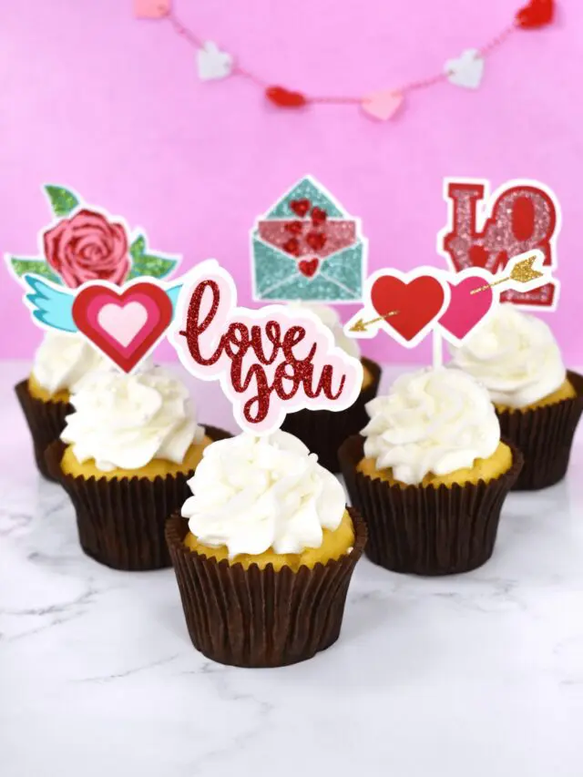 The image shows white cupcakes with handmade cupcake toppers. Create DIY cupcake toppers with your Cricut machine. Follow this tutorial and download seven valentine's day SVG files for making your own cupcake toppers.